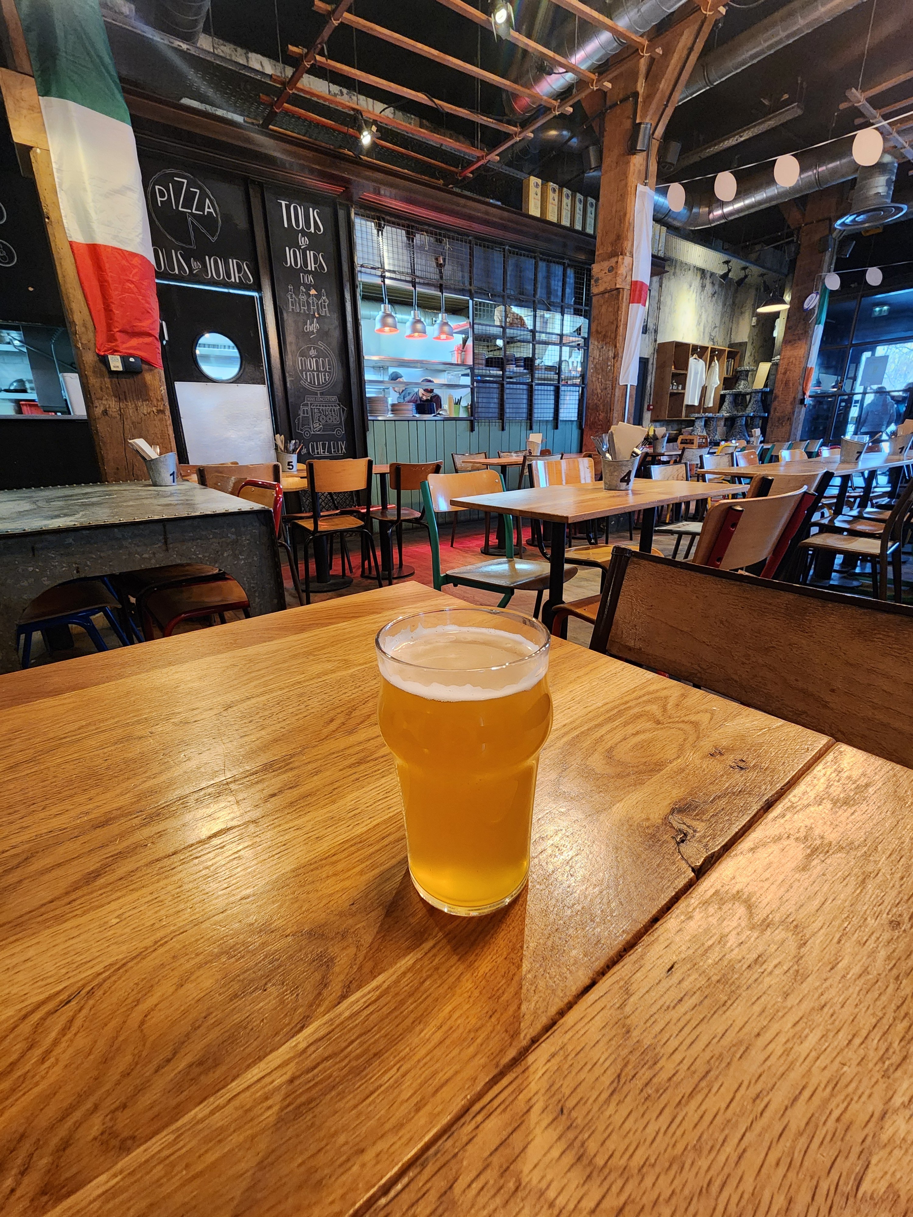 A glass of beer on a table in the foreground, and the kitchen in the back