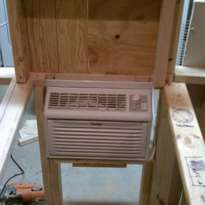 The air conditioner is dryfit in its aperture.  Above it is the back panel of the draft box.  The 2x4s protrude from the wall to form a cleat that the removable box will rest on.